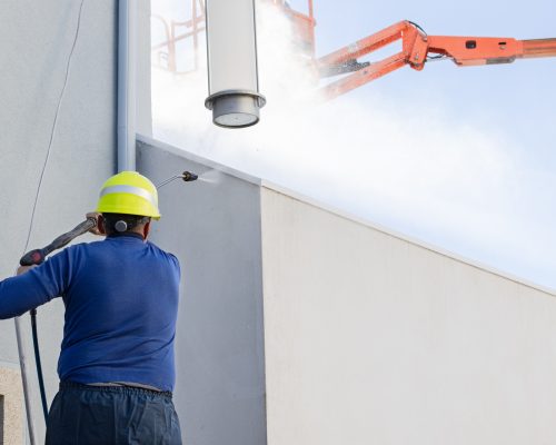 Worker cleaning a building facade with high pressure water jet